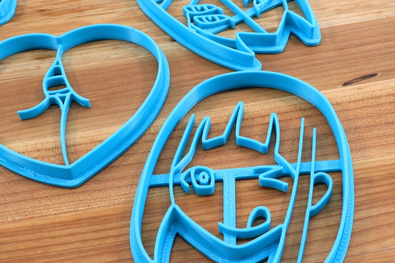 May include: Three blue plastic cookie cutters, one shaped like a heart, one shaped like a face, and one shaped like a flower.