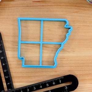 Op de afbeelding: Een blauwe plastic koekjesvormer in de vorm van de staat Arkansas. De vormer is verdeeld in vier secties door lijnen.