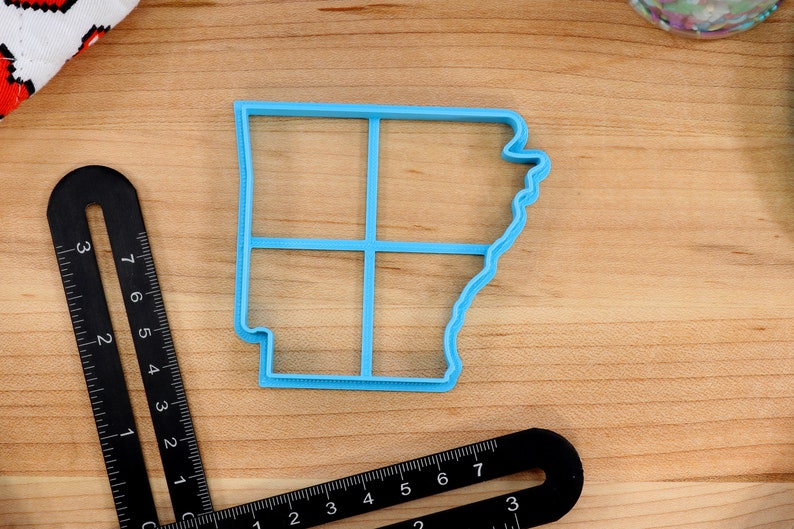 Op de afbeelding: Een blauwe plastic koekjesvormer in de vorm van de staat Arkansas. De vormer is verdeeld in vier secties door lijnen.