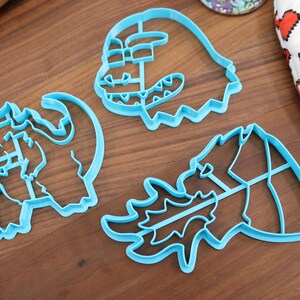 May include: Three blue plastic cookie cutters shaped like dragons. The cutters are on a wooden surface.