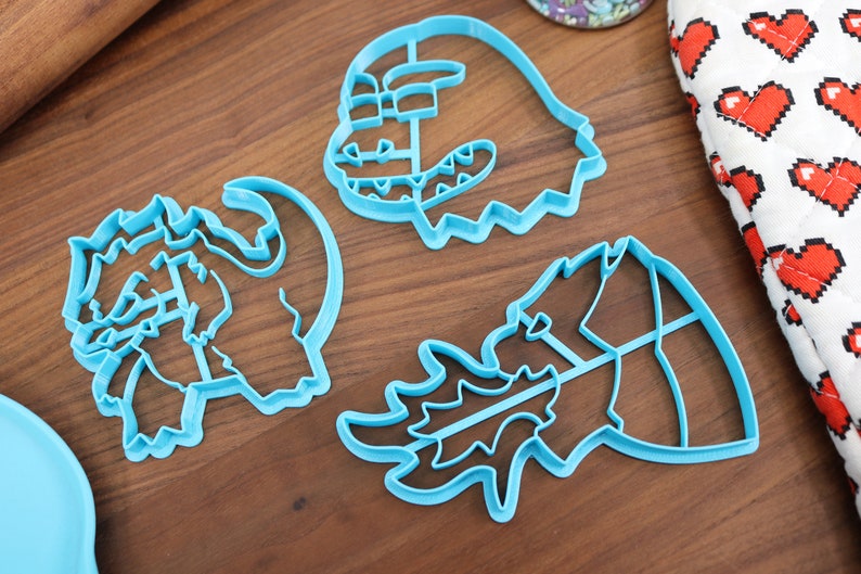 May include: Three blue plastic cookie cutters shaped like dragons. The cutters are on a wooden surface.