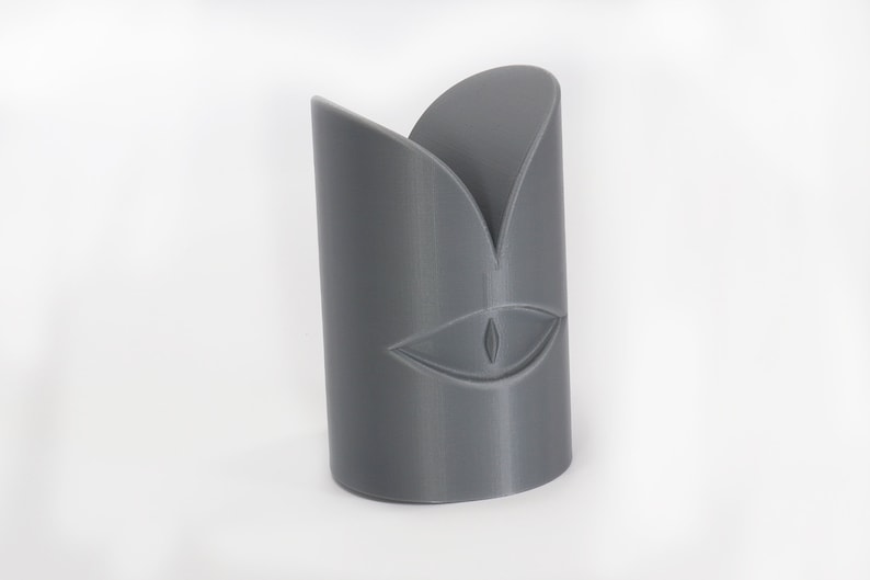 May include: A grey 3D printed sculpture of a face with a single eye and a stylised mouth.