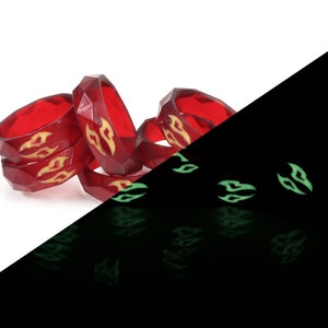 May include: A stack of five red glow-in-the-dark rings with a flame design. The rings are stacked on a white surface and glow green in the dark.
