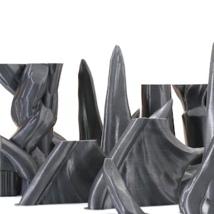 Puede incluir: Una colecci&oacute;n de esculturas abstractas impresas en 3D de color gris con una superficie lisa y texturizada. Las esculturas est&aacute;n dispuestas en fila sobre un fondo blanco.