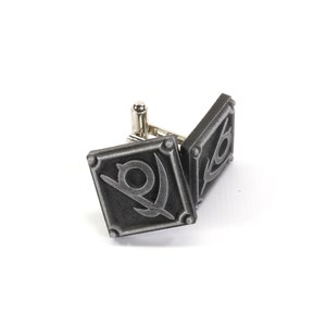 May include: A pair of silver cufflinks with a diamond-shaped design featuring a stylized symbol of a sword and a circle.