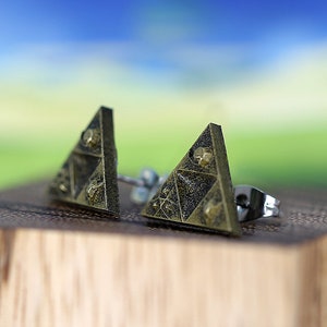 May include: A pair of gold-toned triangle-shaped earrings with a textured surface. The earrings have a silver post and back.