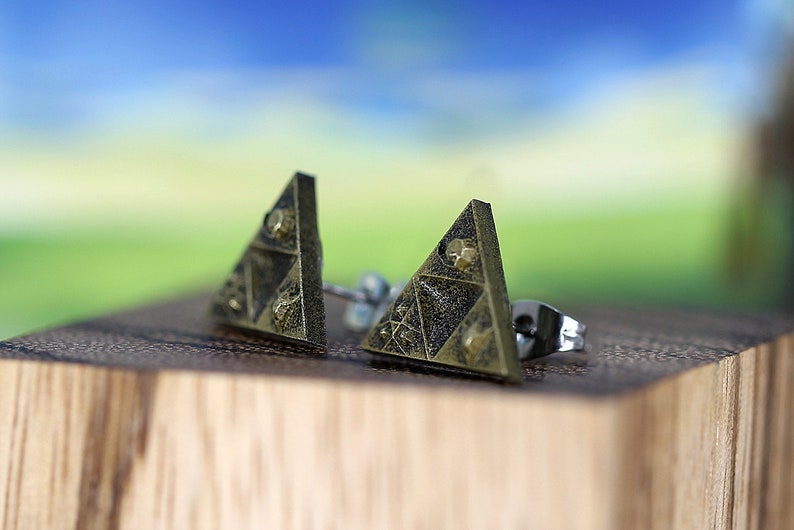 May include: A pair of gold-toned triangle-shaped earrings with a textured surface. The earrings have a silver post and back.