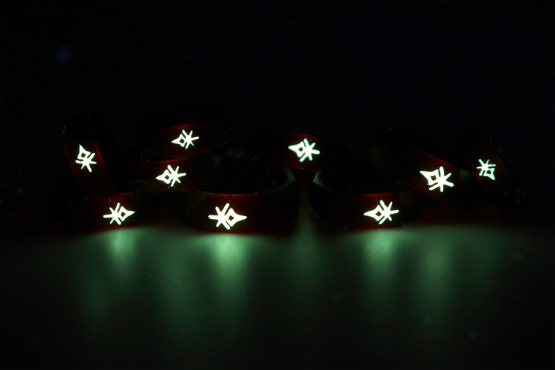 May include: A group of eight red glow-in-the-dark silicone bracelets with a white starburst design. The bracelets are arranged in a semi-circle on a dark surface.