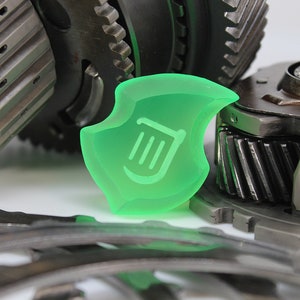 May include: A translucent green shield-shaped object with a white harp symbol, set against a backdrop of various metal gears and mechanical components. The gears are in shades of grey and silver.
