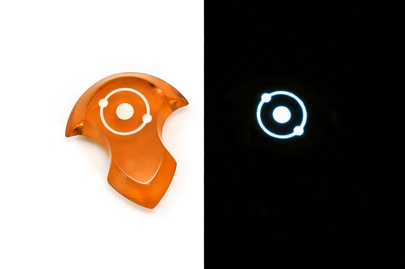 May include: An orange resin pendant with a white atom symbol. The pendant glows in the dark.