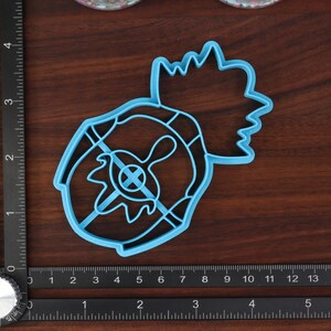 May include: A blue plastic cookie cutter shaped like a pineapple with a detailed design. The cutter is on a wooden surface with a ruler for scale.