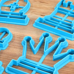 May include: A set of four blue plastic cookie cutters shaped like chess pieces: a king, a queen, a rook, and a pawn. The cutters are on a wooden surface.