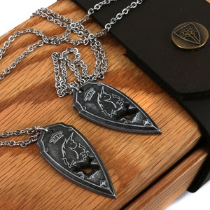 May include: Two silver necklaces with matching pendants in the shape of a shield with a unicorn design. The necklaces are displayed in a wooden box with a black leather flap.