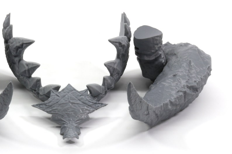 May include: A set of three gray 3D printed dragon teeth, each with a unique shape and texture. The teeth are designed for use in tabletop games or as decorative pieces.