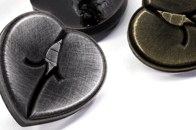 May include: Three heart-shaped metal buttons with a distressed finish. The buttons have a raised design of a broken heart.