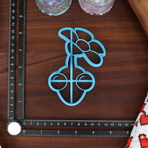 May include: A blue plastic cookie cutter shaped like a flower with a stem and two round eyes.