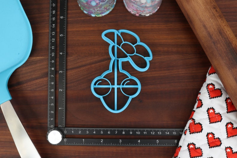 May include: A blue plastic cookie cutter shaped like a flower with a stem and two round eyes.
