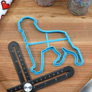 May include: A blue plastic dog-shaped cookie cutter on a wooden surface with a black ruler and a rolling pin.