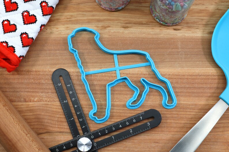 May include: A blue plastic dog-shaped cookie cutter on a wooden surface with a black ruler and a rolling pin.