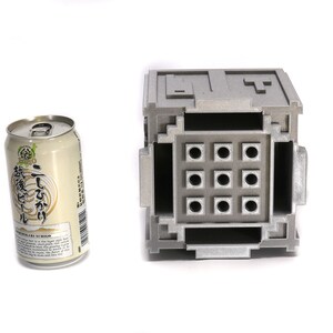 May include: A silver metal box with a grid of nine square holes. The box is about the size of a can of soda.