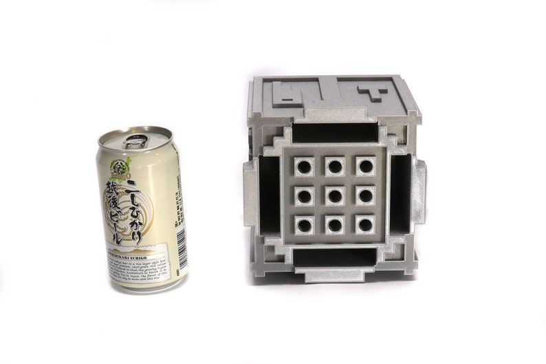 May include: A silver metal box with a grid of nine square holes. The box is about the size of a can of soda.