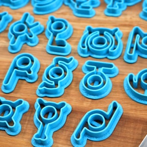 May include: A set of blue plastic cookie cutters shaped like different symbols. The cutters are arranged on a wooden surface.