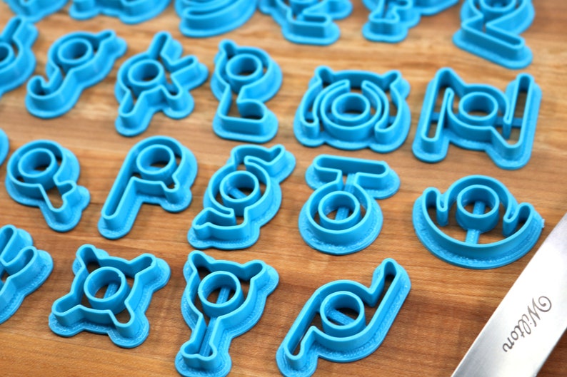 May include: A set of blue plastic cookie cutters shaped like different symbols. The cutters are arranged on a wooden surface.