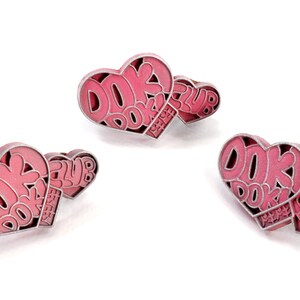 May include: Three pink heart-shaped pins with silver outlines. Each pin features the text "DOK DOK ENERGY CLUB" in a stylized font.