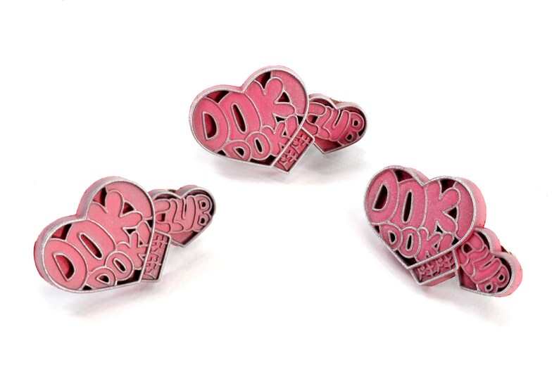May include: Three pink heart-shaped pins with silver outlines. Each pin features the text "DOK DOK ENERGY CLUB" in a stylized font.