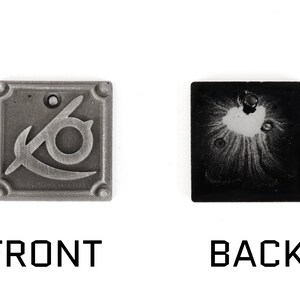 May include: A silver metal charm with a stylized eye and a curved blade design on the front. The back of the charm is black with a silver-colored design.