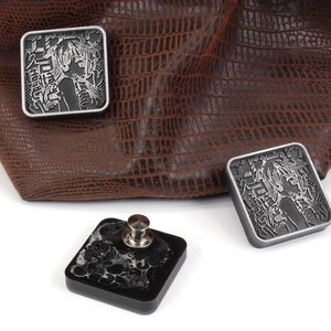 Puede incluir: Tres dados cuadrados de metal con acabado plateado y un dise&ntilde;o grabado de una mujer con texto japon&eacute;s. Los dados est&aacute;n sobre una superficie blanca junto a una bolsa de cuero marr&oacute;n.