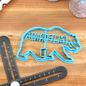 May include: A blue plastic cookie cutter shaped like a California bear with the word "CALIFORNIA" written across the bear's back.