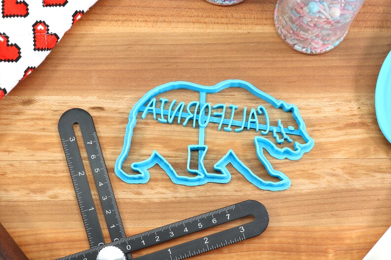 May include: A blue plastic cookie cutter shaped like a California bear with the word "CALIFORNIA" written across the bear's back.