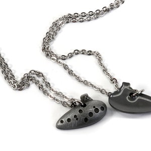 May include: Two silver necklaces with pendants. One pendant is a heart shape and the other is a stylized ocarina.