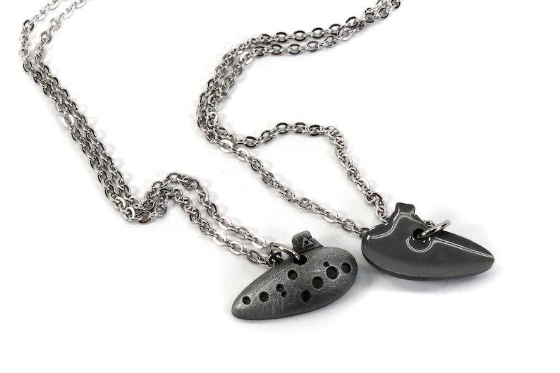 May include: Two silver necklaces with pendants. One pendant is a heart shape and the other is a stylized ocarina.