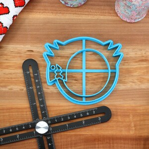 May include: Blue plastic cookie cutter shaped like a cartoon character with a circle in the middle and a fish in its mouth.