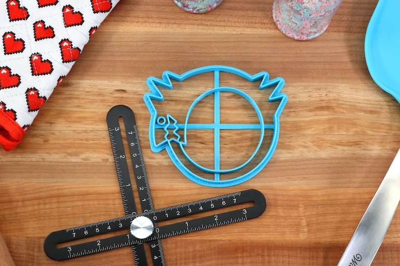 May include: Blue plastic cookie cutter shaped like a cartoon character with a circle in the middle and a fish in its mouth.