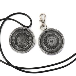 May include: Two silver-toned pendants with a geometric design and a black cord necklace. One pendant is attached to a silver-toned keychain.