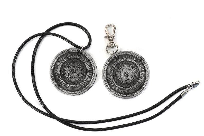 May include: Two silver-toned pendants with a geometric design and a black cord necklace. One pendant is attached to a silver-toned keychain.