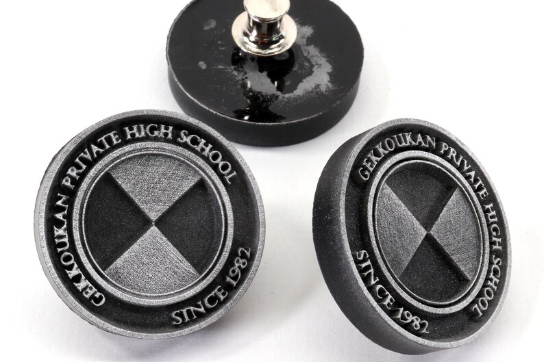 Pu&ograve; includere: Tre spille in metallo nero e argento con il testo "Gekkoukan Private High School Since 1982" e un design a X stilizzato.