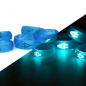 May include: A group of six blue silicone rings with a white arrow design. The rings glow bright teal in the dark.