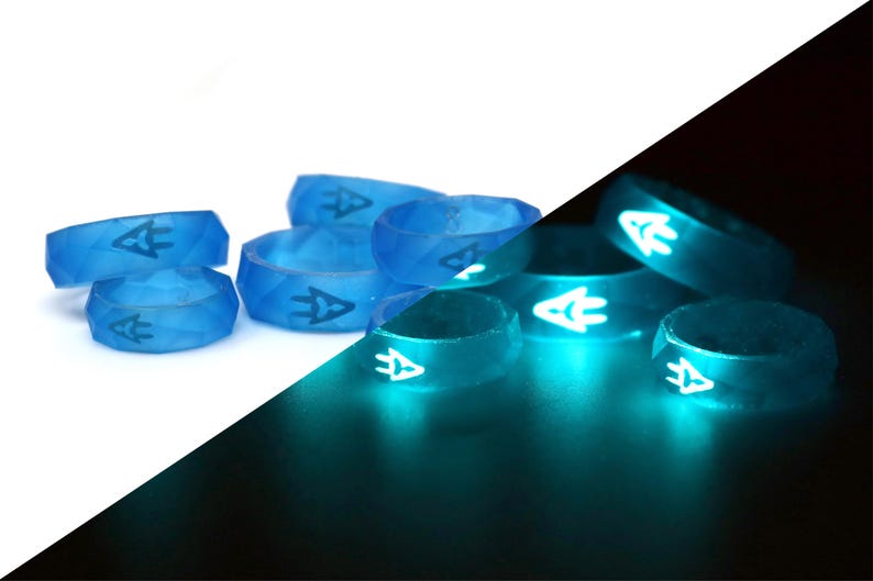 May include: A group of six blue silicone rings with a white arrow design. The rings glow bright teal in the dark.