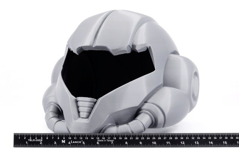 May include: A gray 3D printed helmet with a futuristic design. The helmet has a large visor and a series of tubes and pipes extending from the sides.