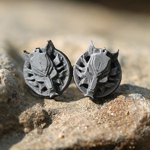 Op de afbeelding: Een paar zilverkleurige oorbel studs met een wolfskop ontwerp. De wolfskop is omgeven door een cirkelvormig ontwerp met een textuur.
