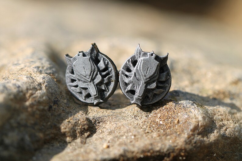 Op de afbeelding: Een paar zilverkleurige oorbel studs met een wolfskop ontwerp. De wolfskop is omgeven door een cirkelvormig ontwerp met een textuur.