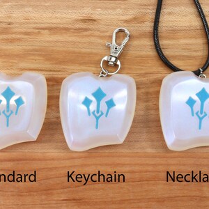 May include: Three versions of a white iridescent pendant with a blue stylized design. The pendant is shown as a standard piece, a keychain, and a necklace.
