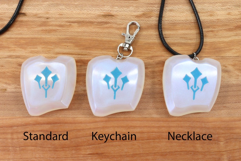 May include: Three versions of a white iridescent pendant with a blue stylized design. The pendant is shown as a standard piece, a keychain, and a necklace.