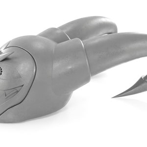 May include: A gray plastic toy with a menacing expression, featuring a large eye with a speaker grille, sharp teeth, and two curved horns. The toy has a textured surface and a sharp point at the end of each horn.
