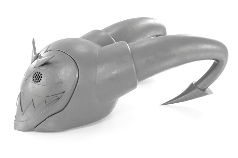 May include: A gray plastic toy with a menacing expression, featuring a large eye with a speaker grille, sharp teeth, and two curved horns. The toy has a textured surface and a sharp point at the end of each horn.
