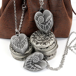 May include: Three silver heart-shaped pendants with a crosshatch design and a small circle in the center. The pendants are on chains and are hanging from a brown leather pouch.